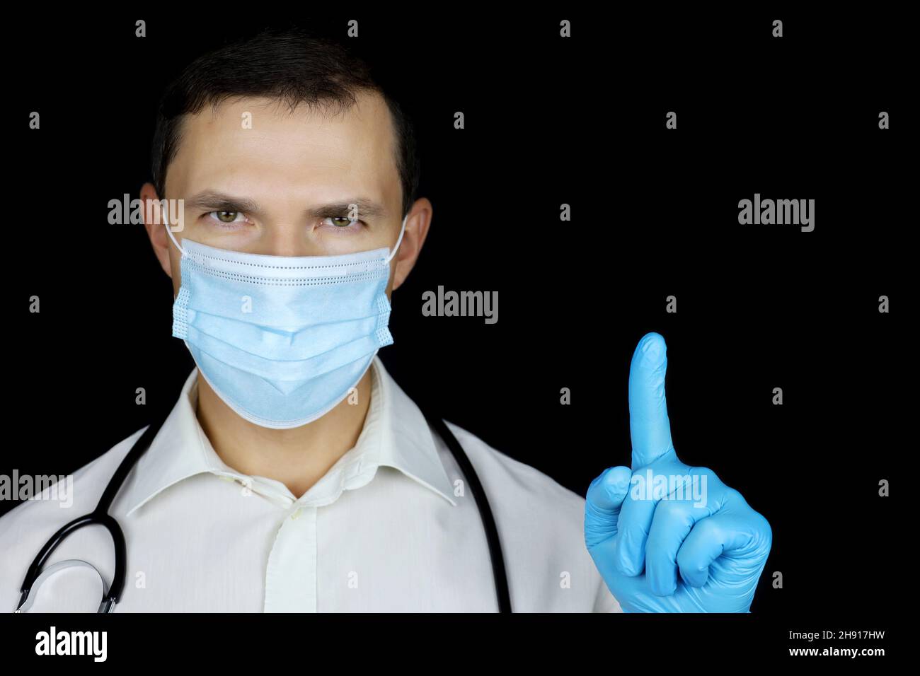 Doctor in disposable face and medical gloves mask points up with his finger. Concept of call for participation, health care, coronavirus protection Stock Photo