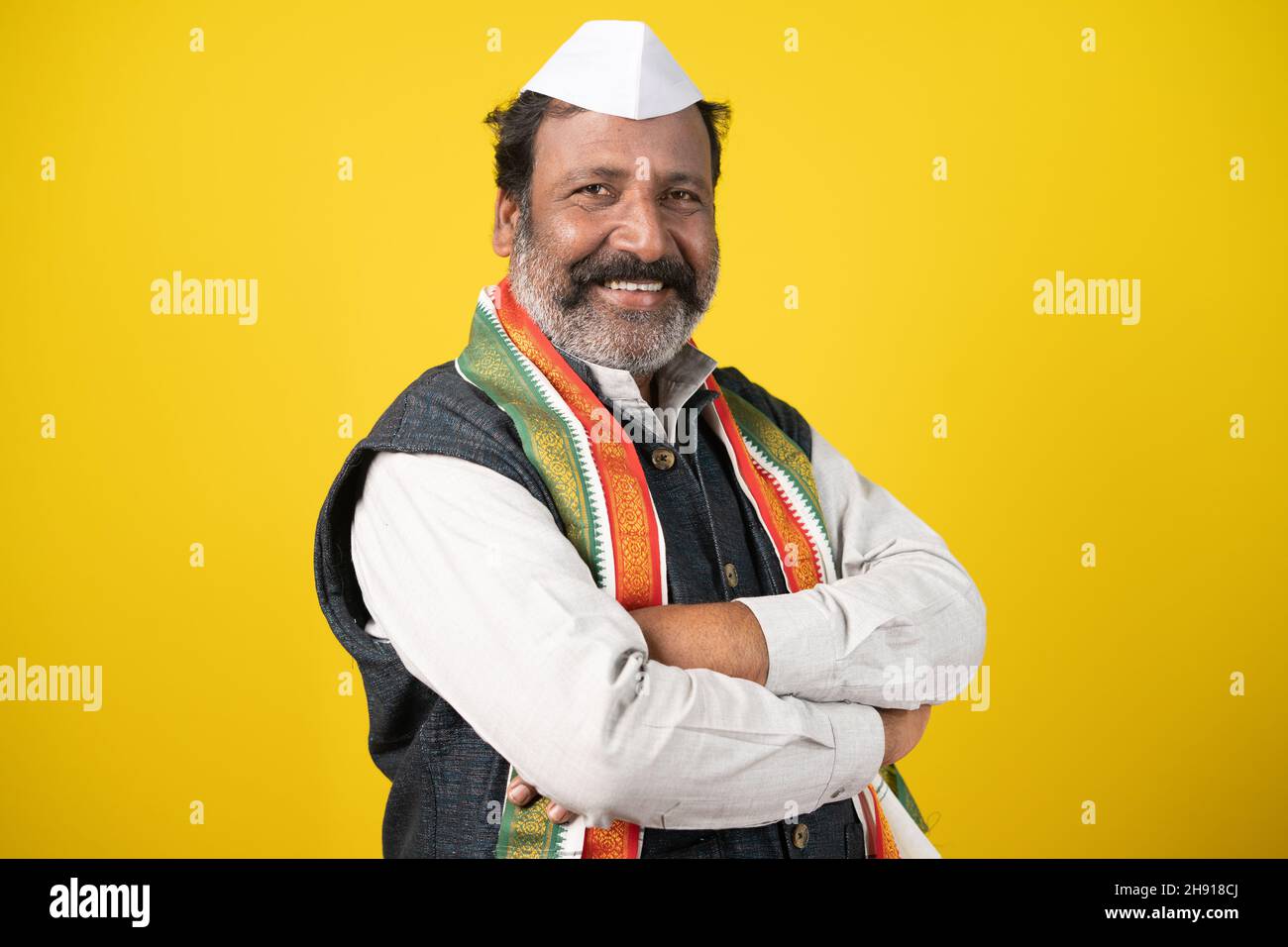 Confident senior politician looking at camera by crossing arms on yellow background - concept of positive expression and successful lawmaker or leader Stock Photo