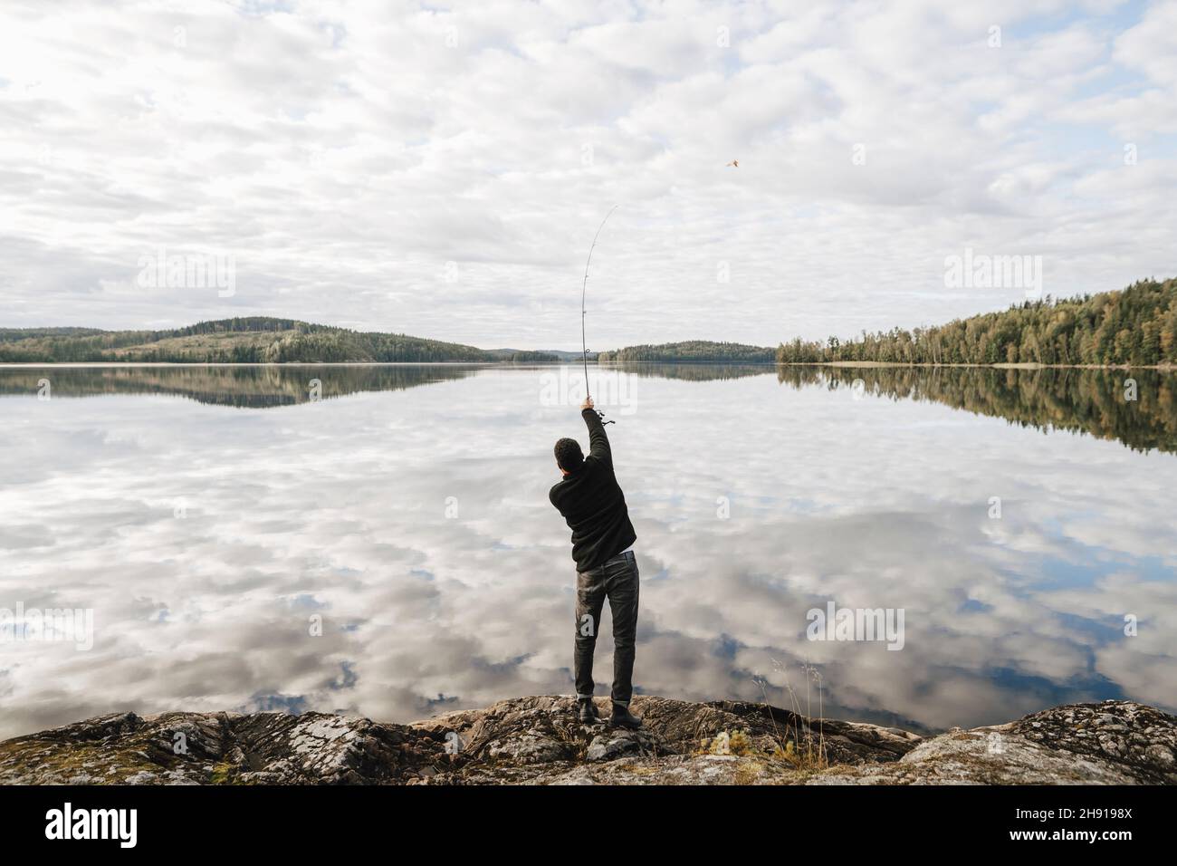 Rear view of man fishing in lake during vacation Stock Photo