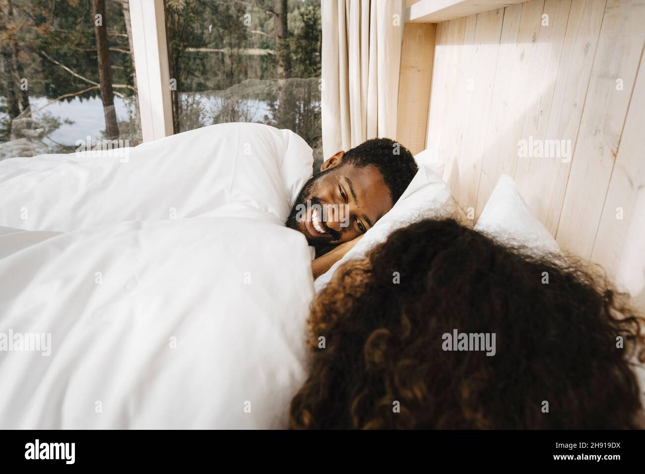 Happy man looking at girlfriend while lying on bed in hotel Stock Photo
