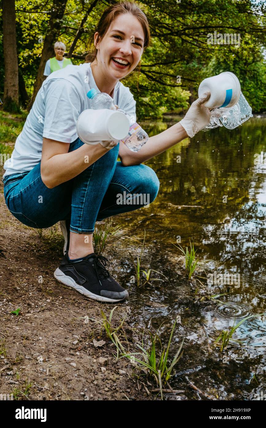 Portrait of smiling female volunteer with plastic waste by pond Stock Photo