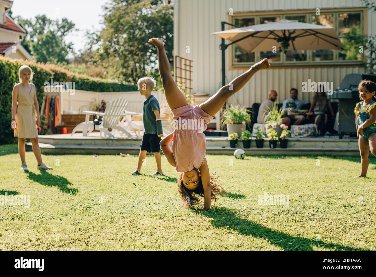 Girl doing cartwheel while playing with friends in backyard on sunny day Stock Photo