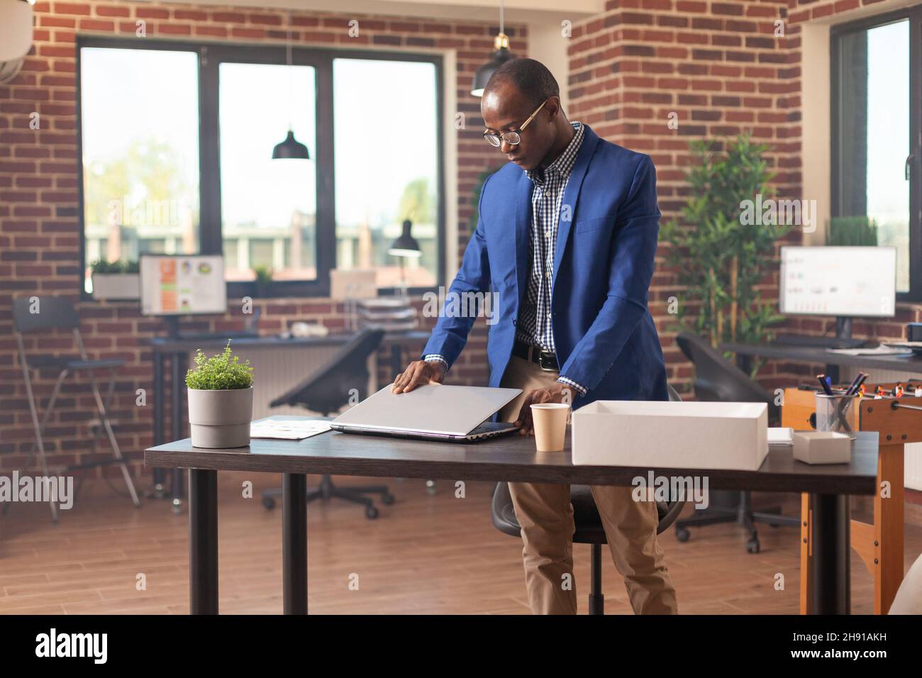 African american man gathering belongings in box after getting fired from business workplace. Frustrated person preparing to leave work after being discharged and dismissed by manager. Stock Photo