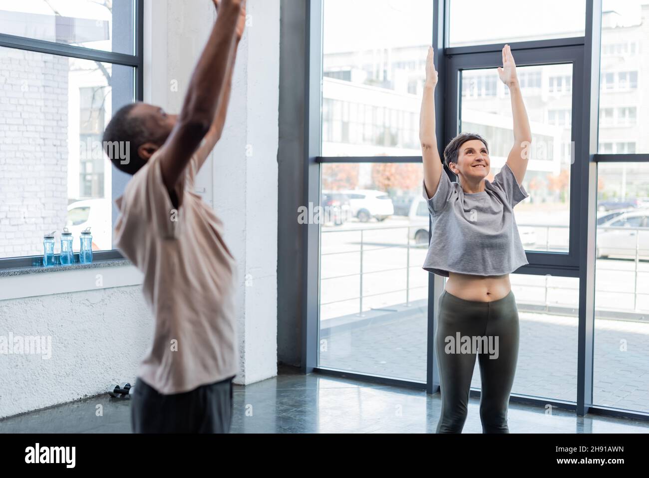 Cheerful senior woman standing in mountain pose near african american man in sports center Stock Photo