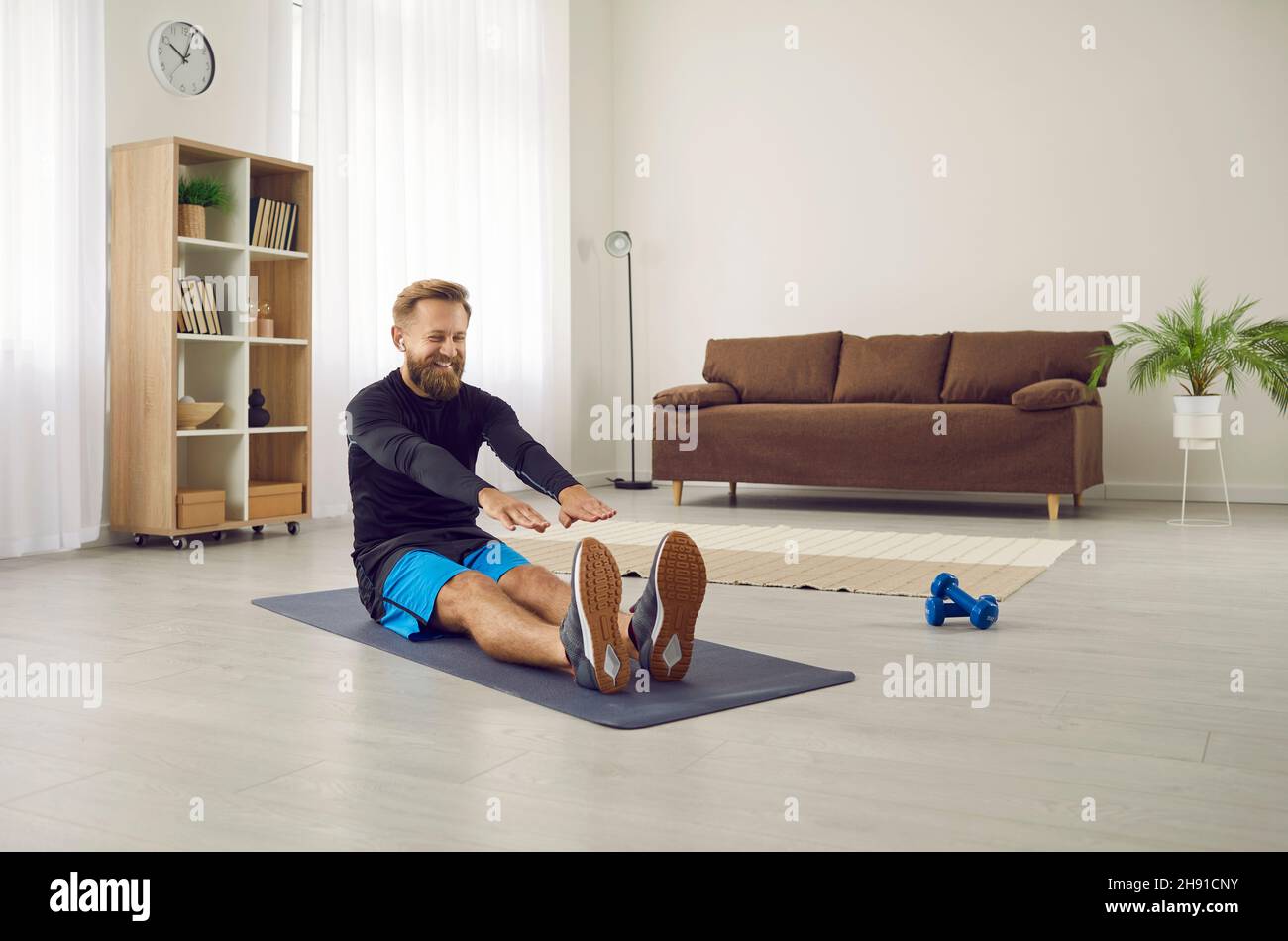 Happy sports man plays sports at home in morning and talks using wireless headphones. Stock Photo