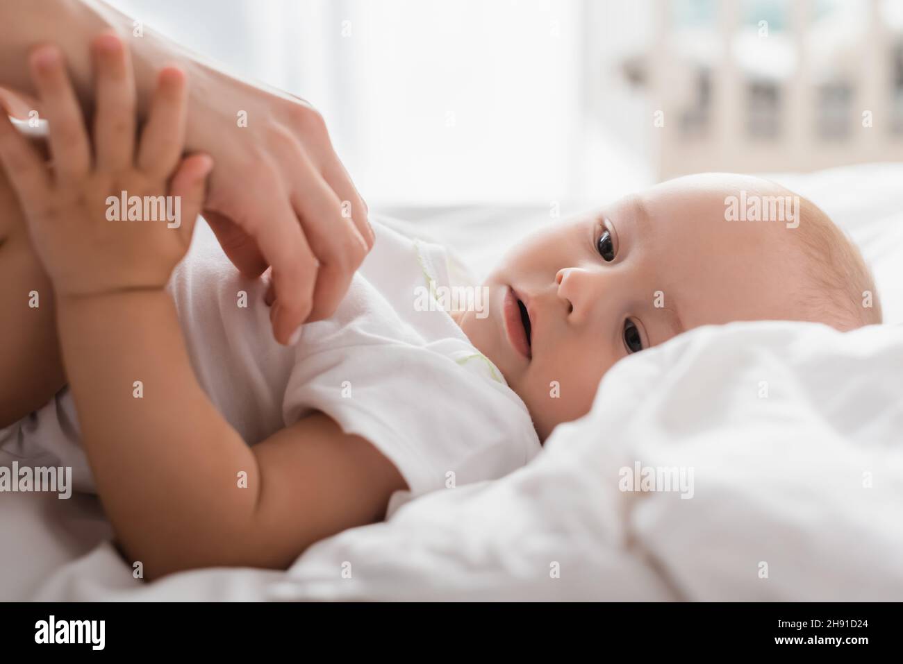 little-boy-touching-hand-of-mother-while-lying-on-white-bedding-stock