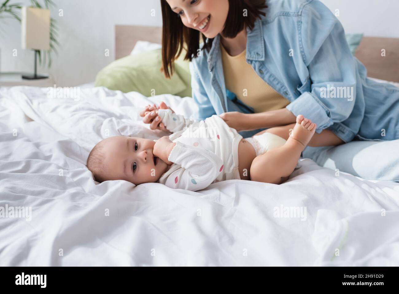 toddler kid holding hand in mouth while lying on bed near cheerful