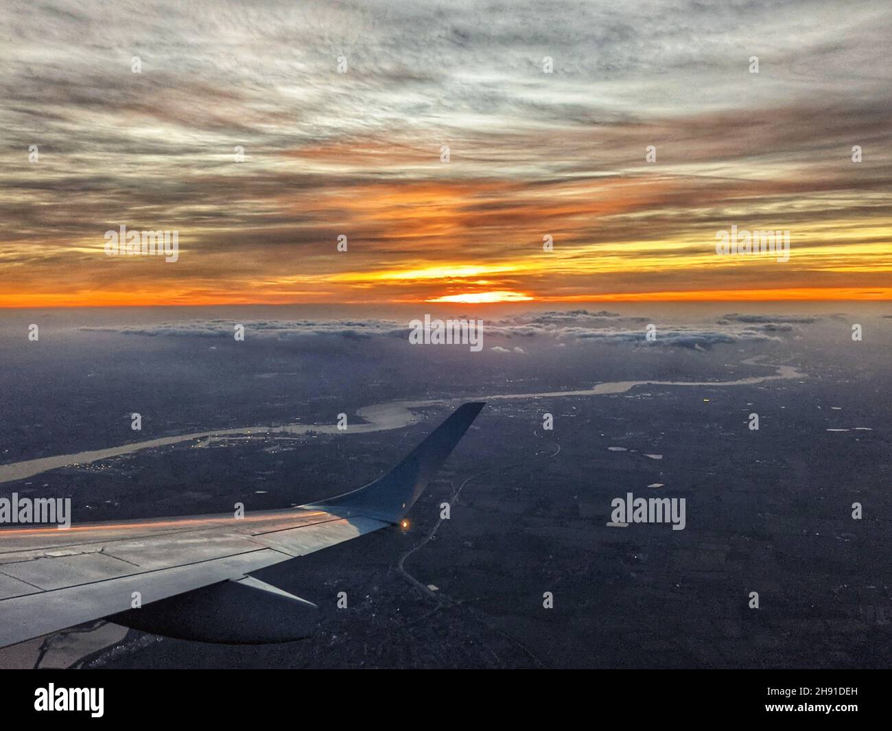 The sun sets in an orange sky over London with the River Thames clearly visible in this photo taken from an aircraft. Stock Photo