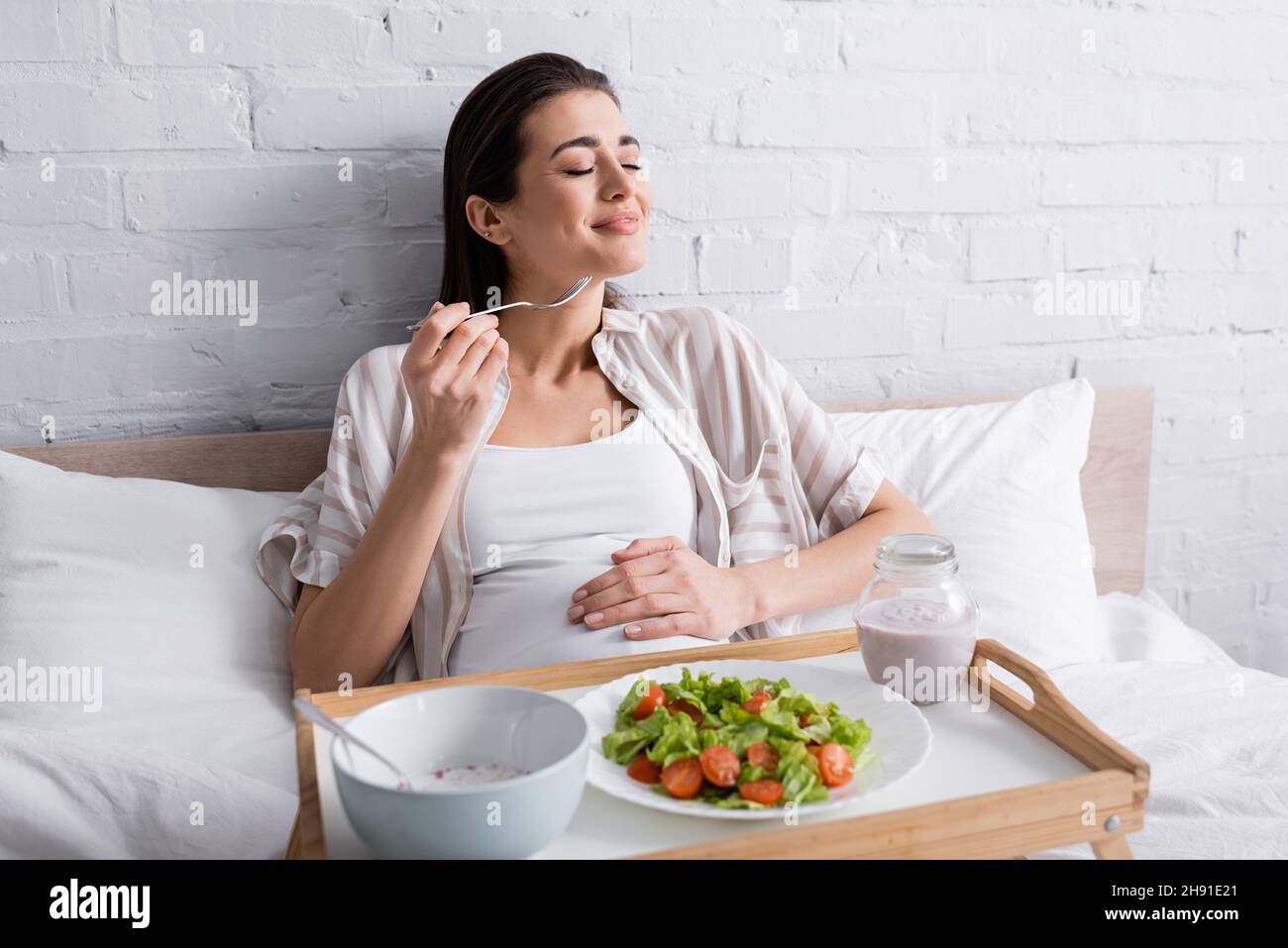 cheerful pregnant woman holding fork near tasty meal on tray Stock