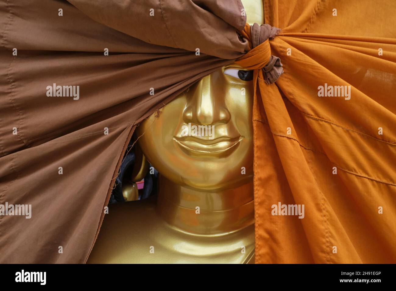 Buddha statue at a factory for Buddhist objects in Bamrung Muang Rd., Bangkok, Thailand, one eye peering out from behind an orange & brown cloth cover Stock Photo