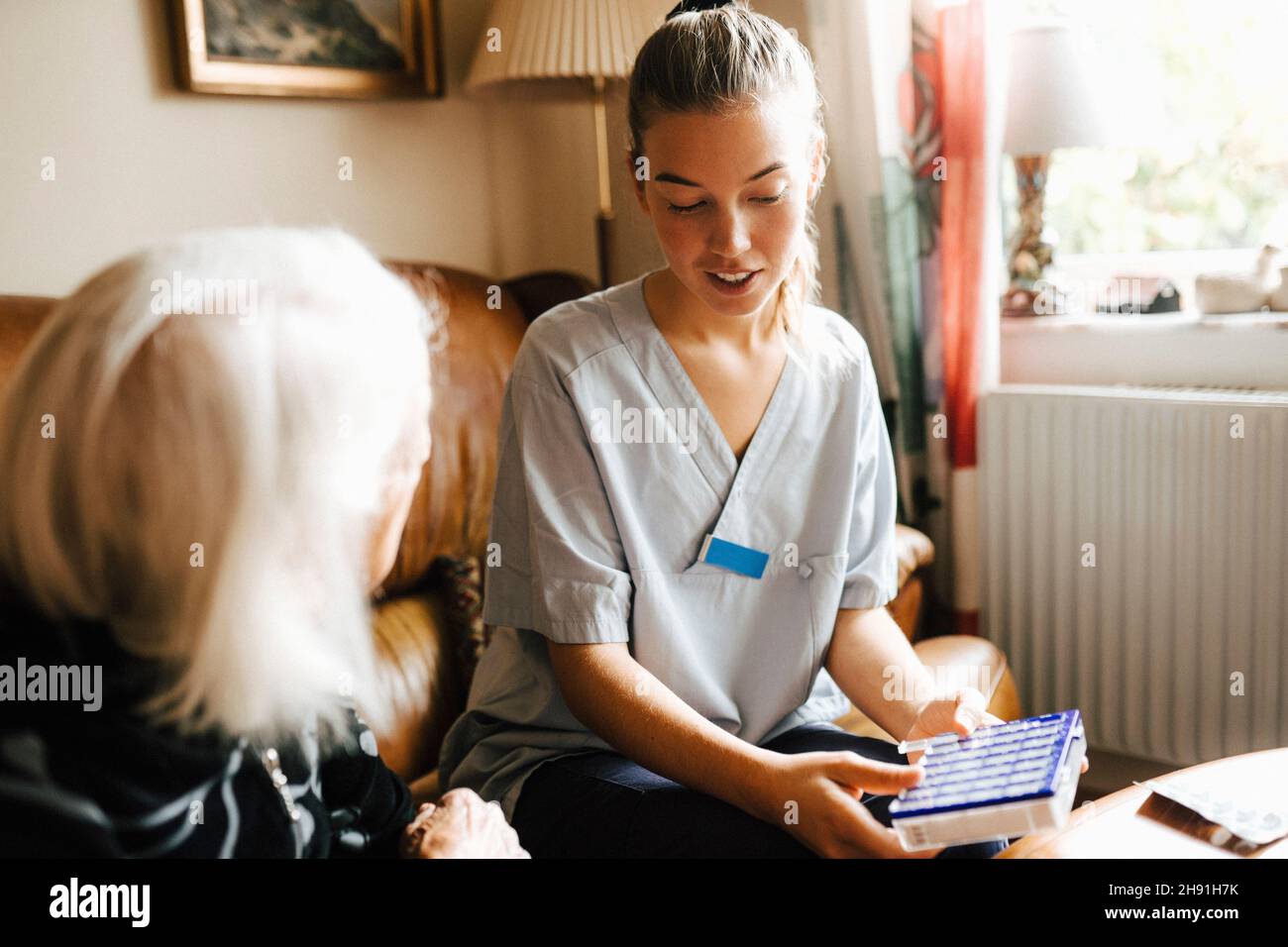 Female healthcare with medicine box talking with senior woman in living room Stock Photo