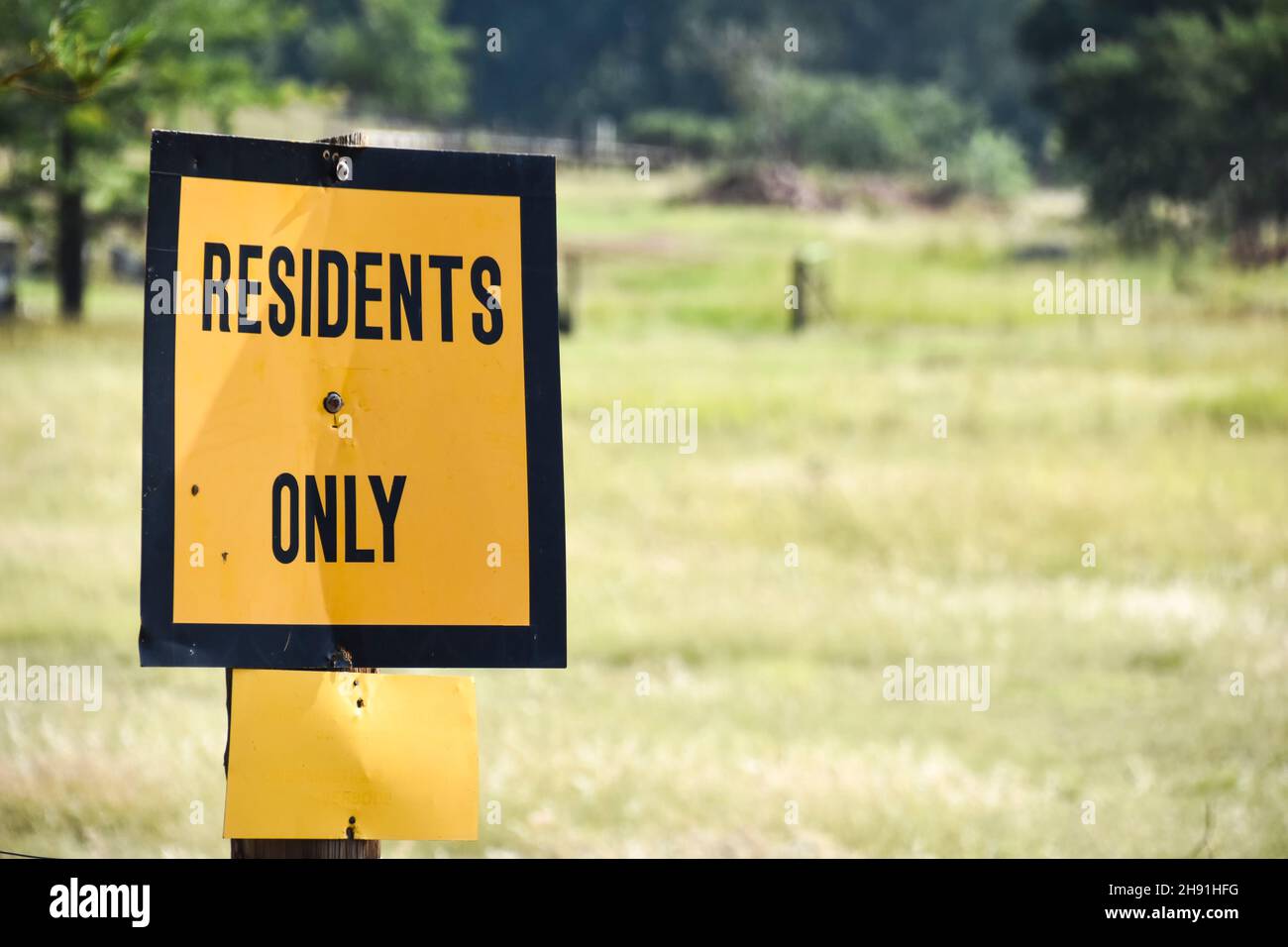 A bright yellow sign saying residents only with a black thick border against the backdrop of a meadow restricting access to third parties to the area Stock Photo