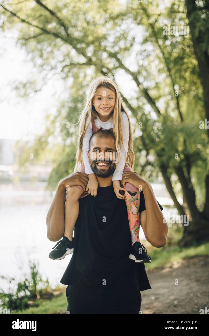 portrait of father carrying daughter on shoulder in park 2H91J1P