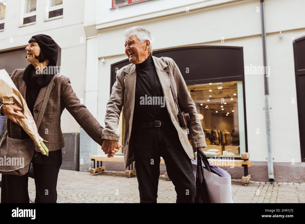 Smiling senior man holding hands of woman while walking on street in city Stock Photo