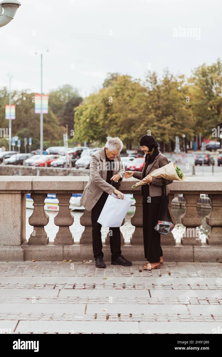 Elderly couple peeking in shopping bag while standing on bridge in city Stock Photo