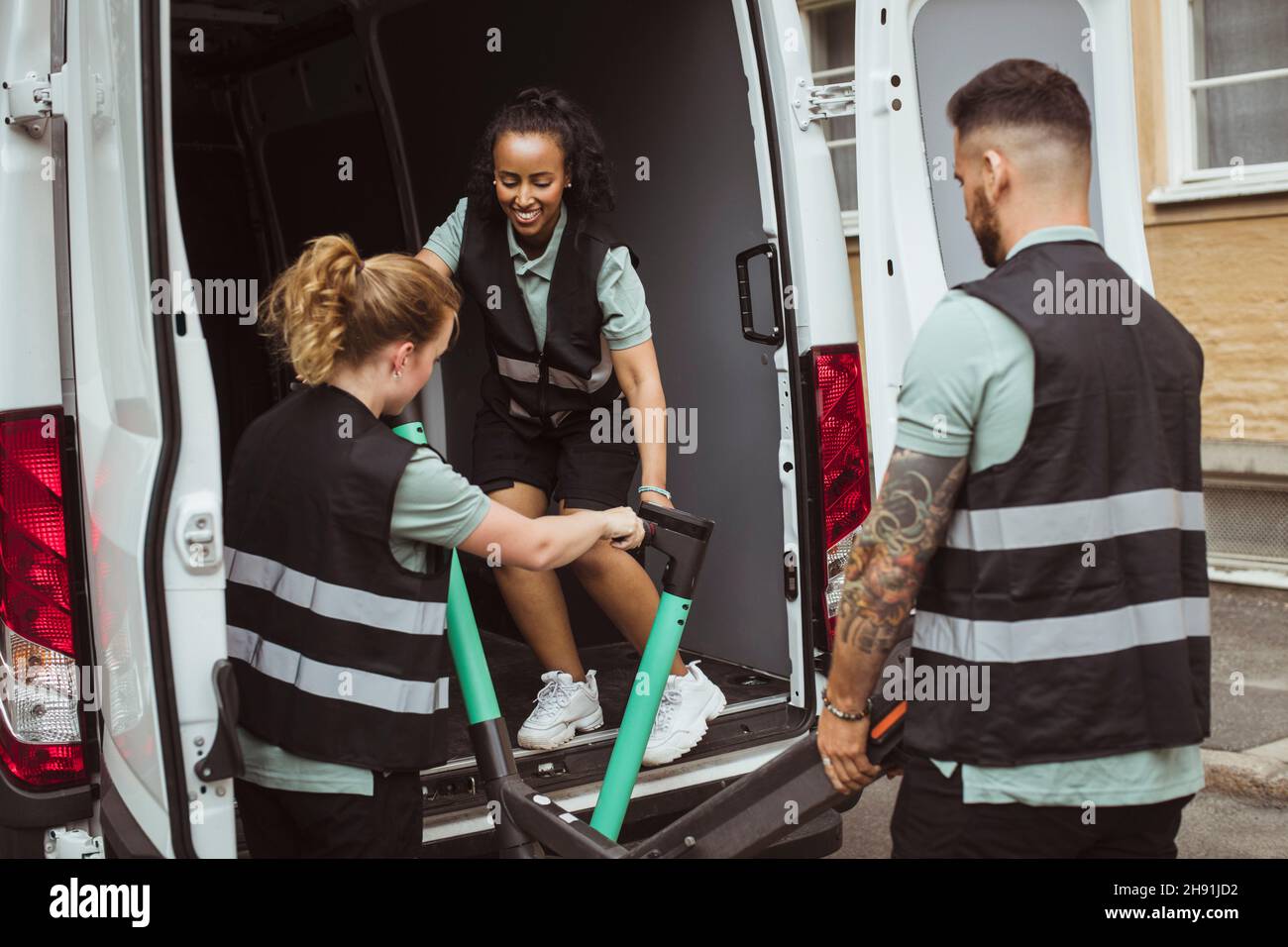 Delivery woman helping male and female coworkers while loading electric push scooter in van Stock Photo