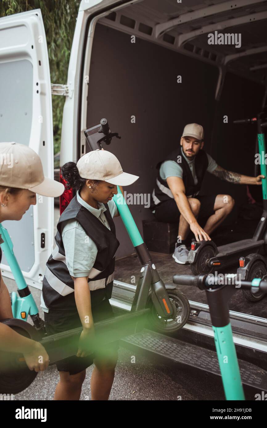 Female delivery workers loading electric push scooters in van Stock Photo