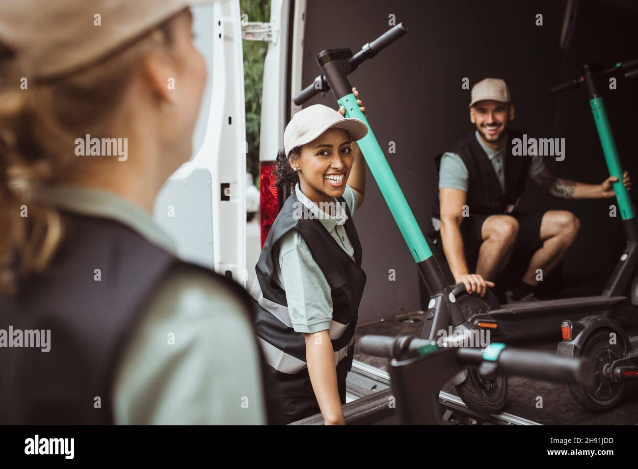 Happy female and male coworkers loading electric push scooter in delivery van Stock Photo