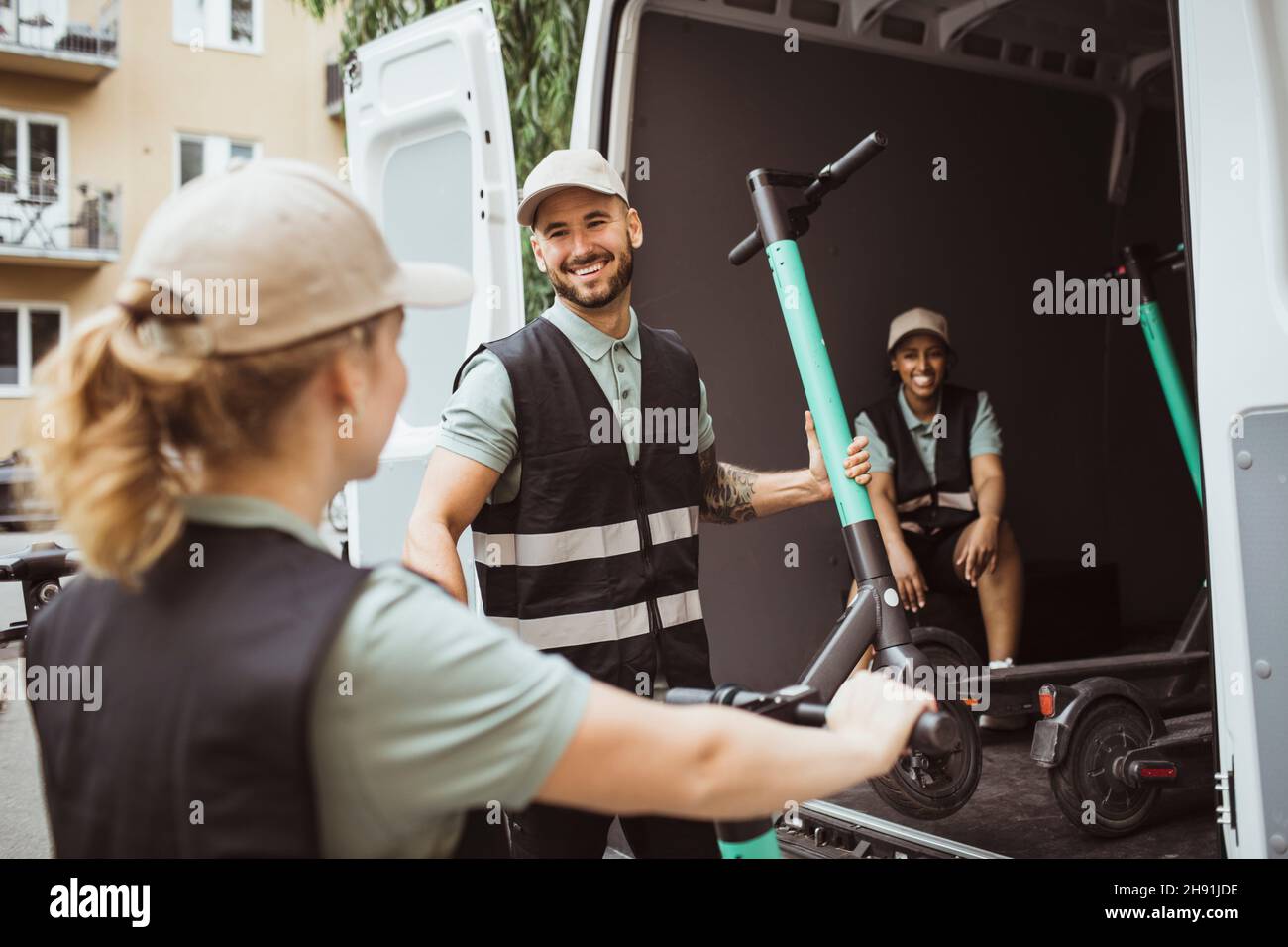 Smiling male worker talking with female coworker while loading push scooter in delivery van Stock Photo