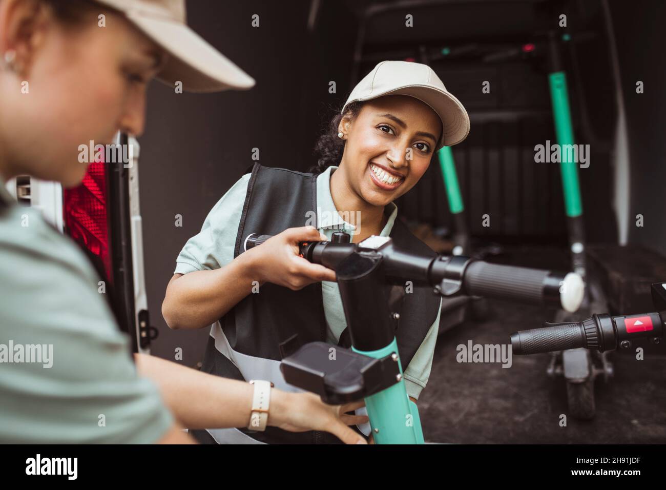 Portrait of delivery woman loading push scooter with female coworker in van Stock Photo