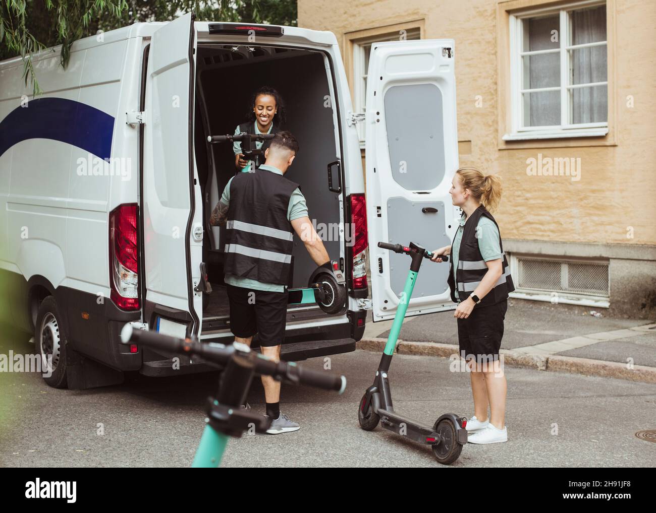 Female and male workers loading electric push scooters in delivery van Stock Photo