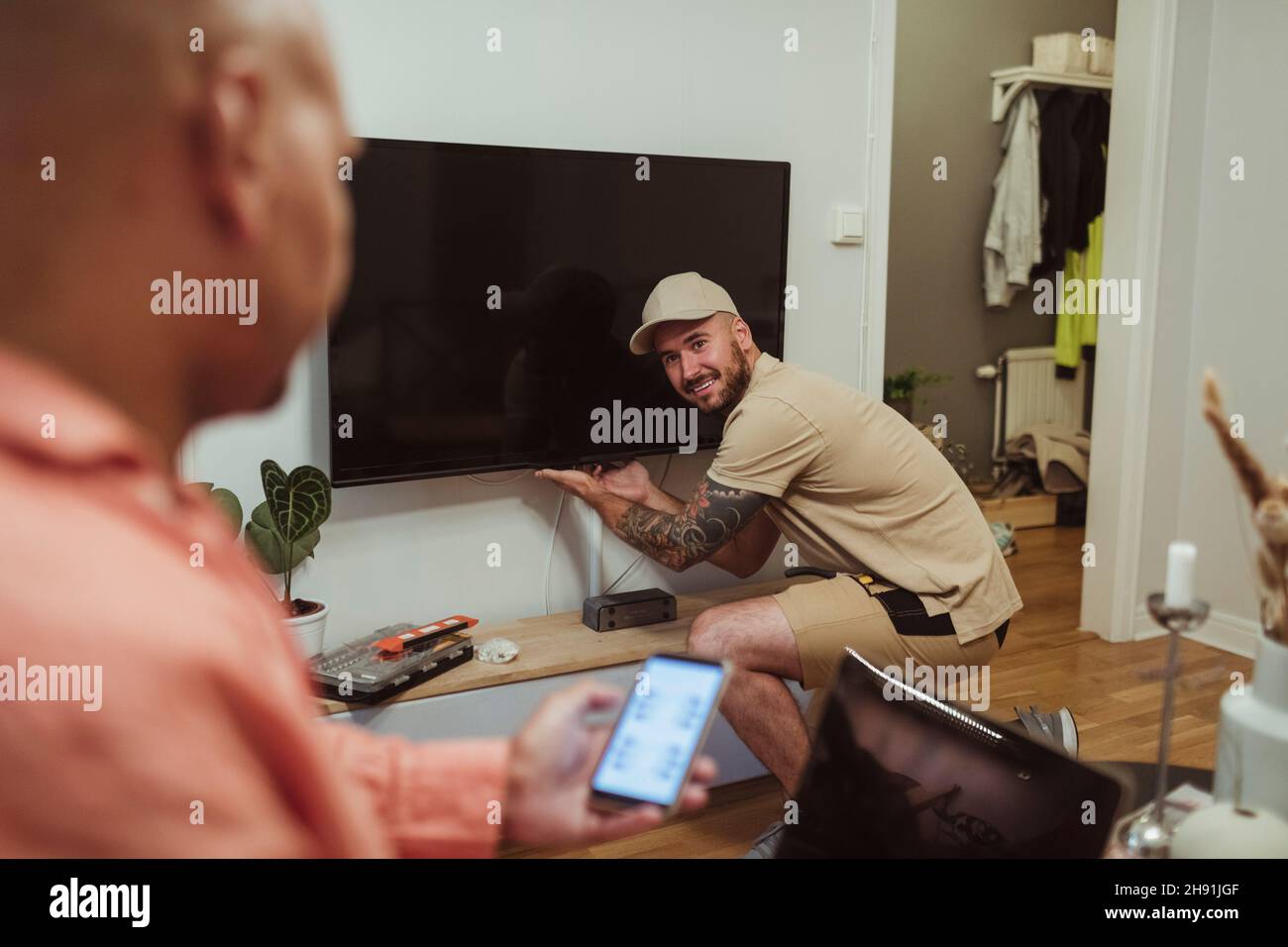 Smiling male technician looking at mature man using smart phone in living room Stock Photo