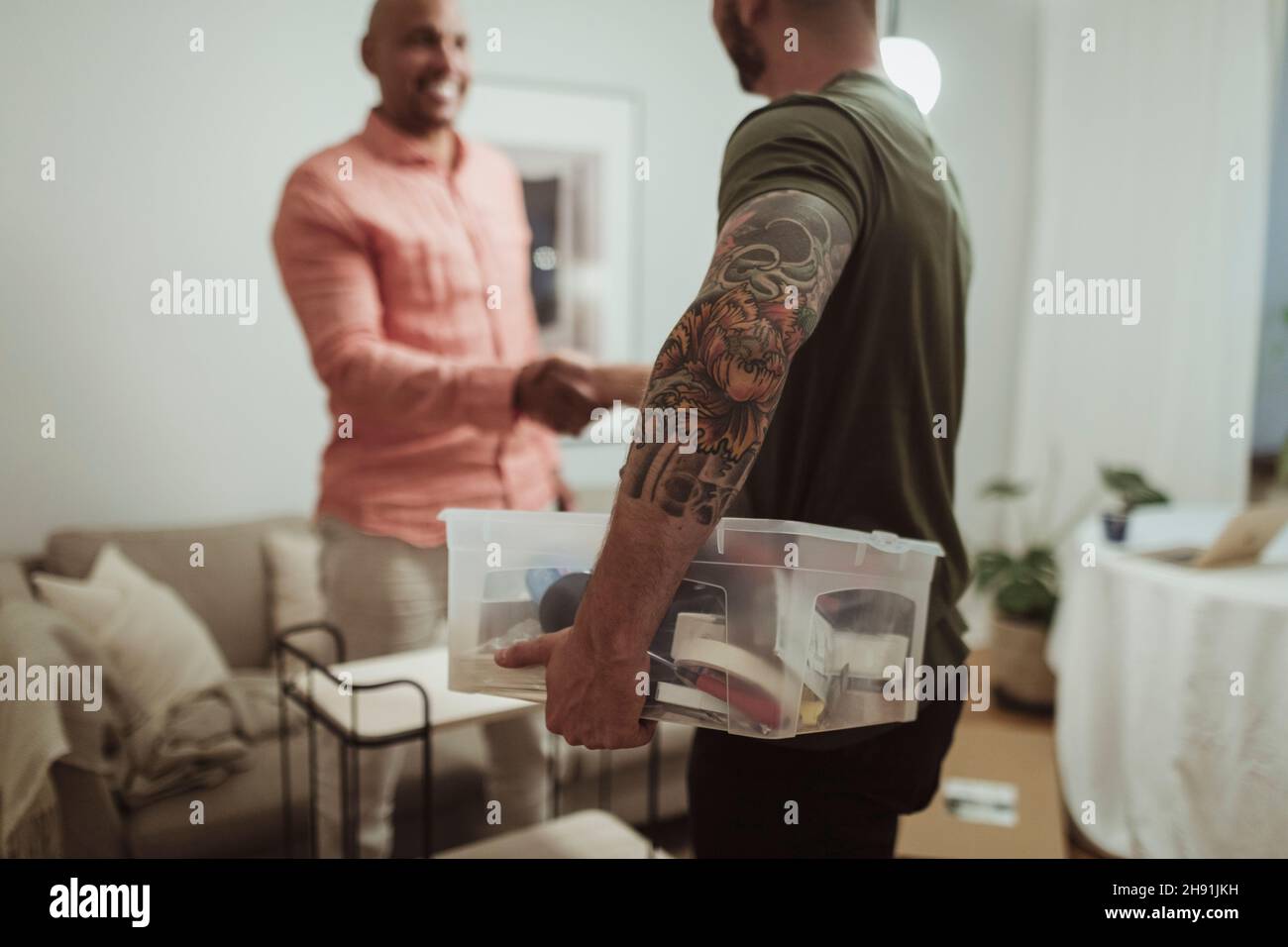 Male craftsperson holding toolbox while doing handshake with customer at home Stock Photo