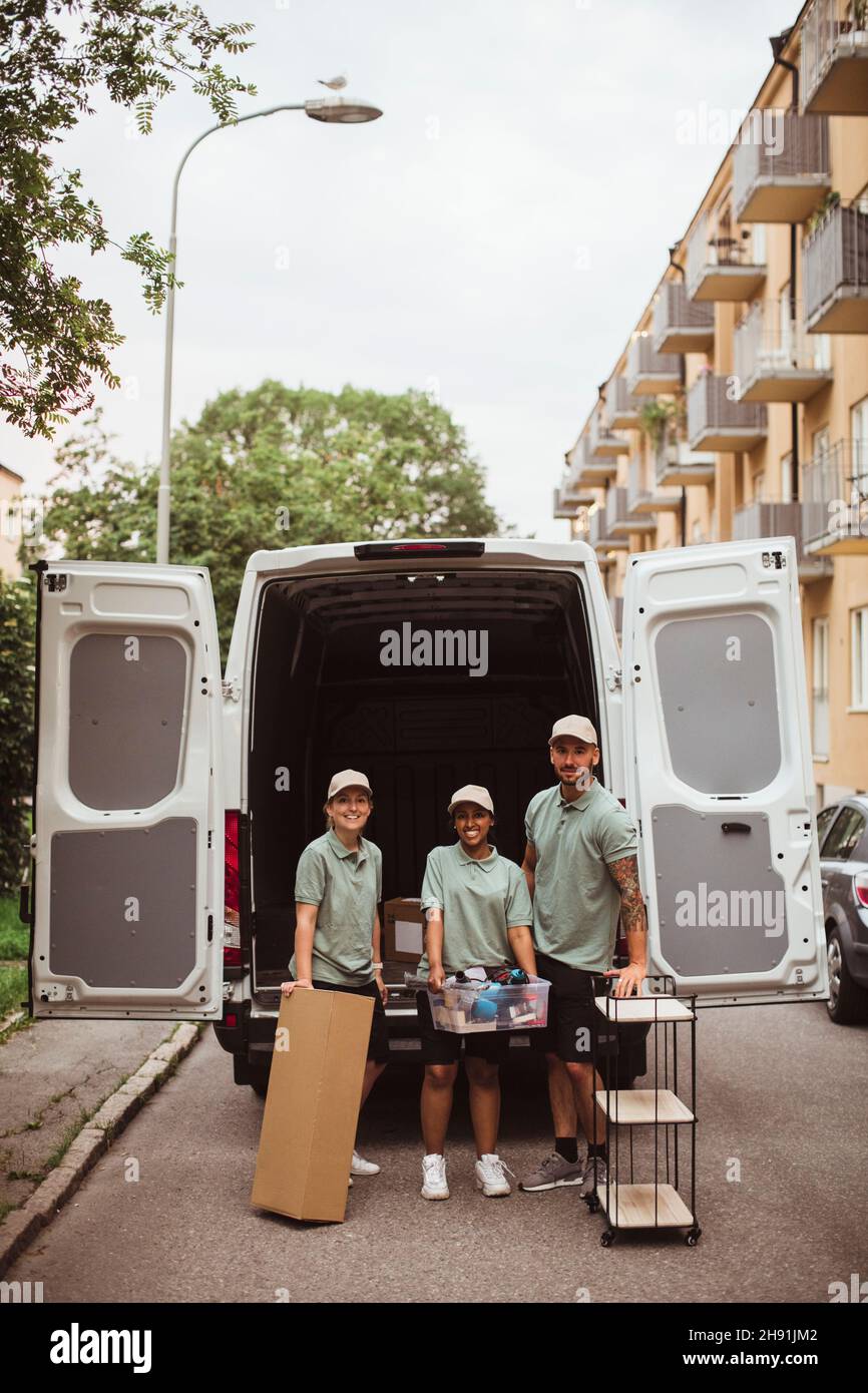 Portrait of delivery coworkers with box and rack against van Stock Photo