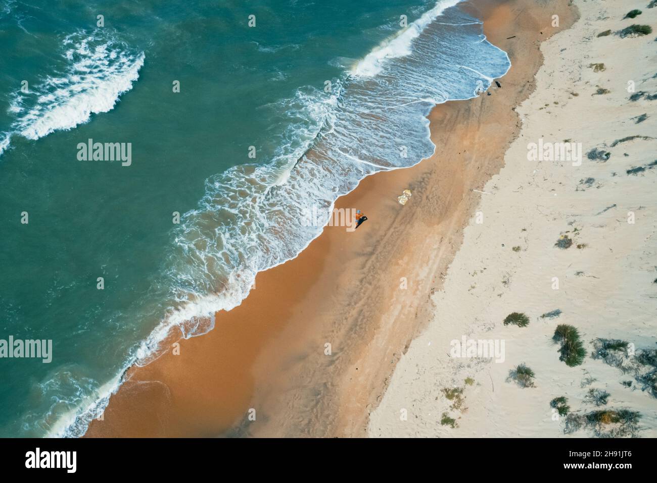 Aerial shot of seashore and crashing waves. Beautiful sandy beach and amazing turquoise tropical sea waters. Perfect summer seascape. Stock Photo