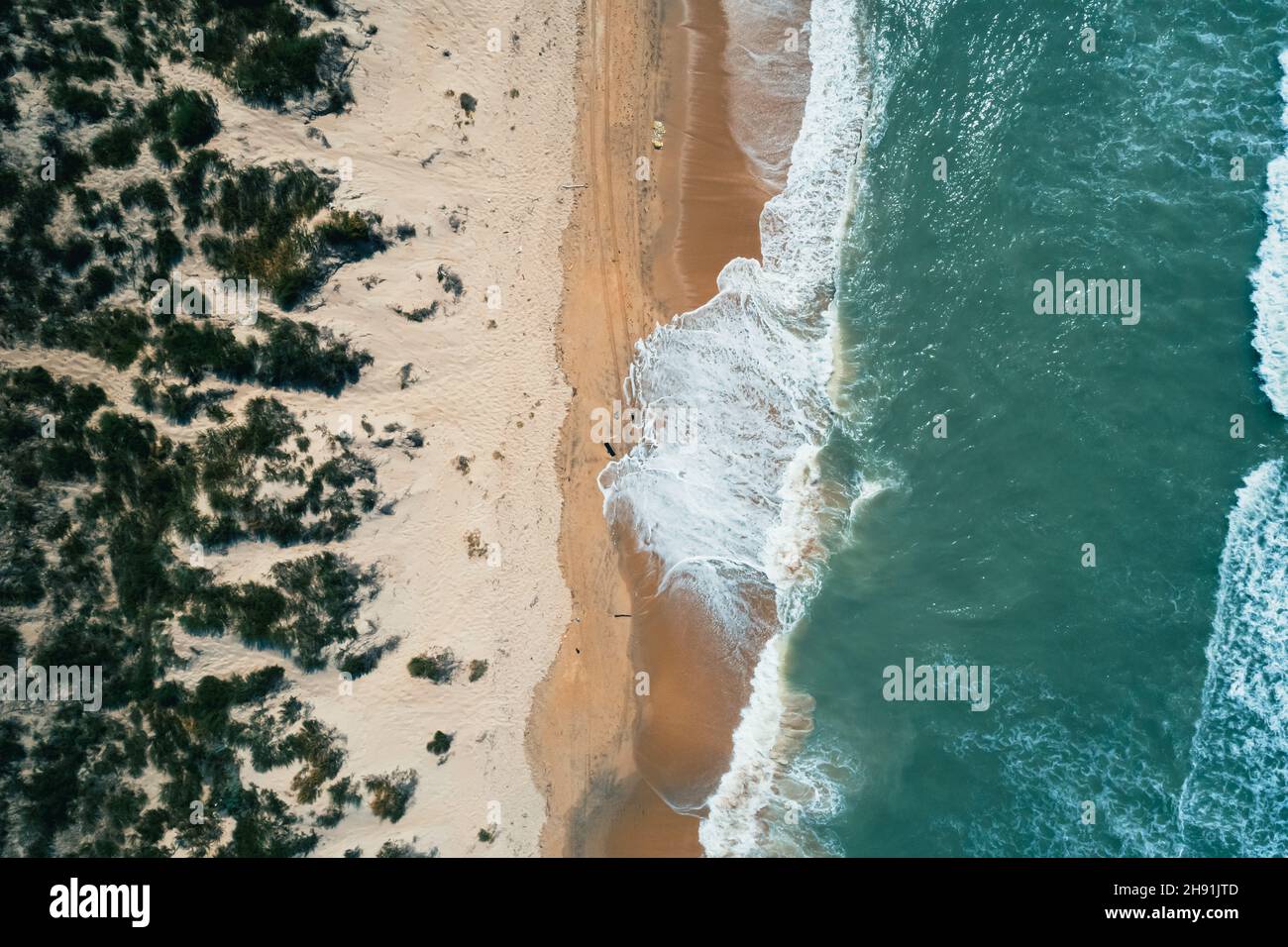 Aerial top down shot of seashore and crashing waves. Beautiful sandy beach and amazing turquoise tropical sea waters. Perfect summer seascape. Stock Photo