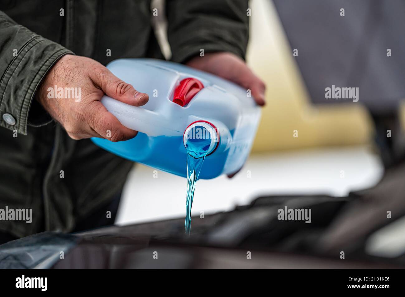 driver refilling the blue nonfreezing windshield washer liquid in the