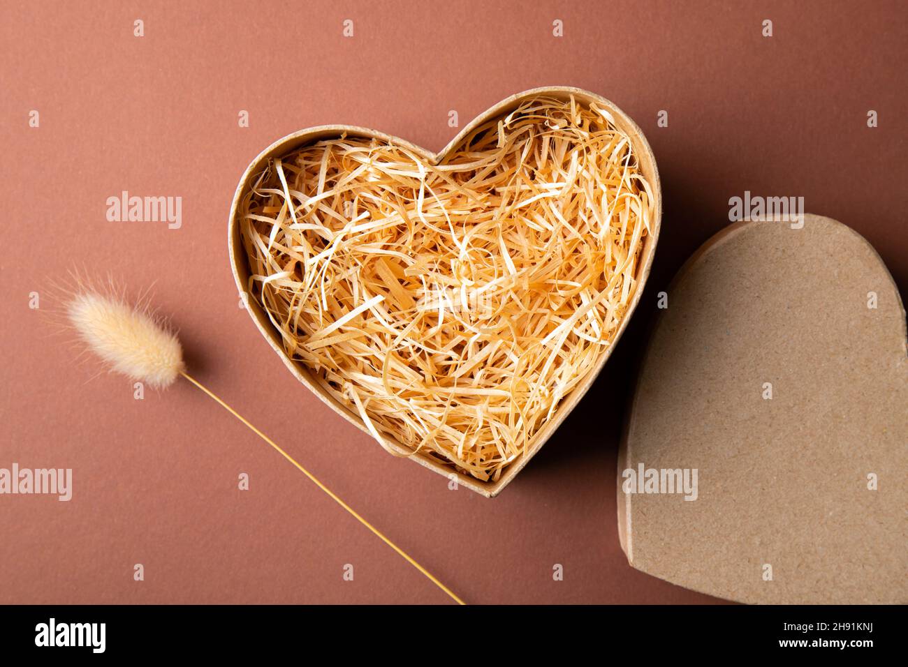 Top view of natural color open heart shape cardboard box with shredded wood excelsior for filling inside, pastel brown background. Natural sustainable Stock Photo