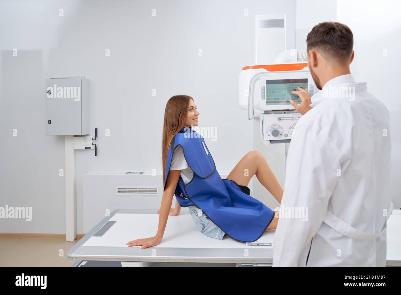 Side view brunette woman smiling wearing blue robe on procedure of ultrasound. Back view using usg equipment starting diagnostic. Concept of modern method of medicine. Stock Photo