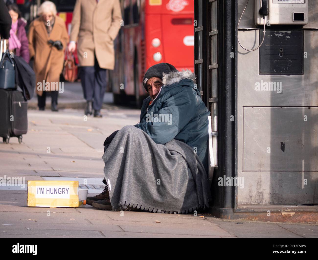 Rich poor divide inequality, male beggar with I'm Hungry sign, begs in Mayfair London as affluent well dressed people walk by Stock Photo