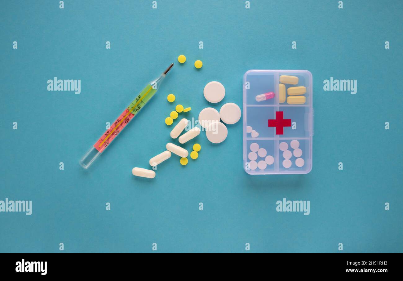 Capsules and tablets are in a pill organizer box on a blue background next to the thermometer. The concept of medicine.Nephrology, glomerulonephritis, Stock Photo