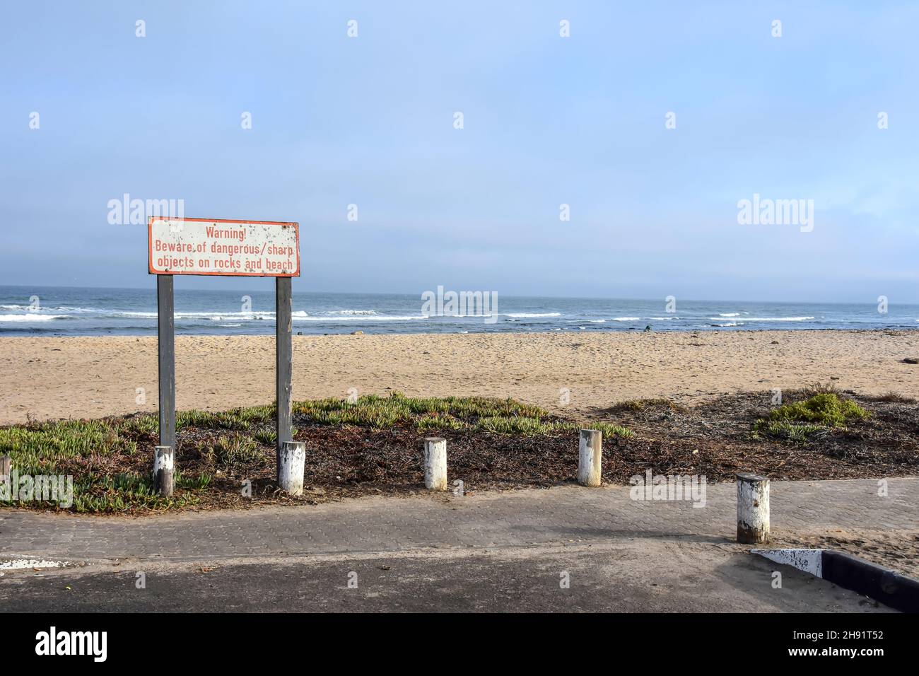 A sign in Swakopmund Namibia Southern Africa at the Atlantic Ocean warning about sharp and dangerous objects on sand and rocks at the beach Stock Photo