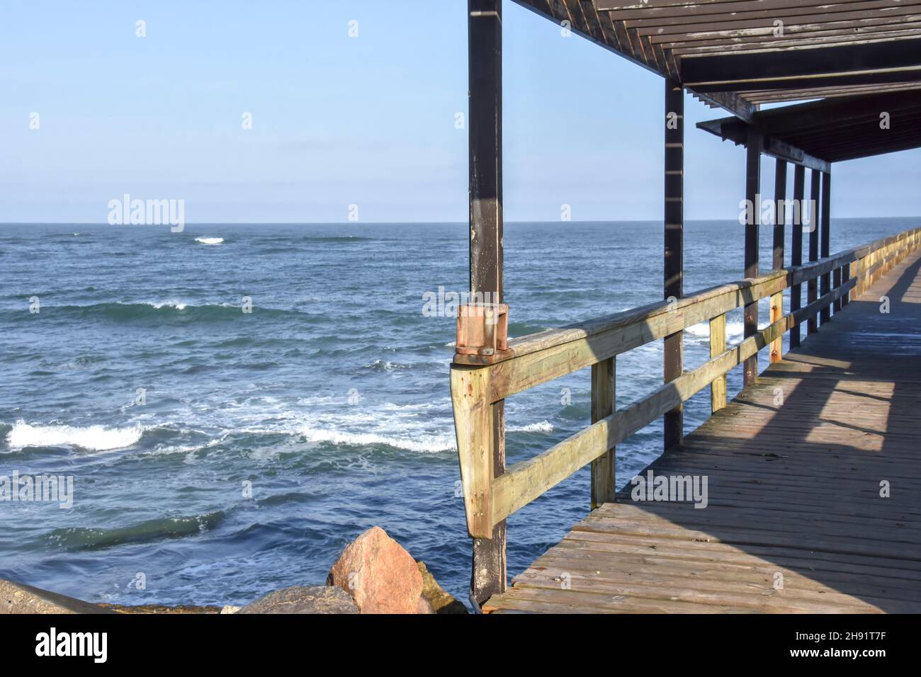 The jetty near the beach of Swakopmund Namibia Southern Africa in the early morning sun at the Atlantic Ocean against a blue sky Stock Photo