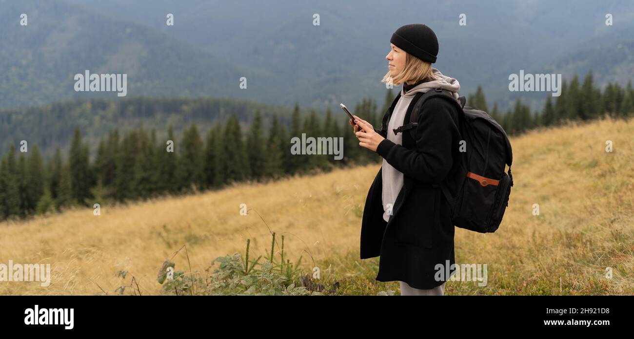 girl standing on top of a mountain using a mobile phone, tourist on a background of mountains with a smartphone, mockup for a text message Stock Photo