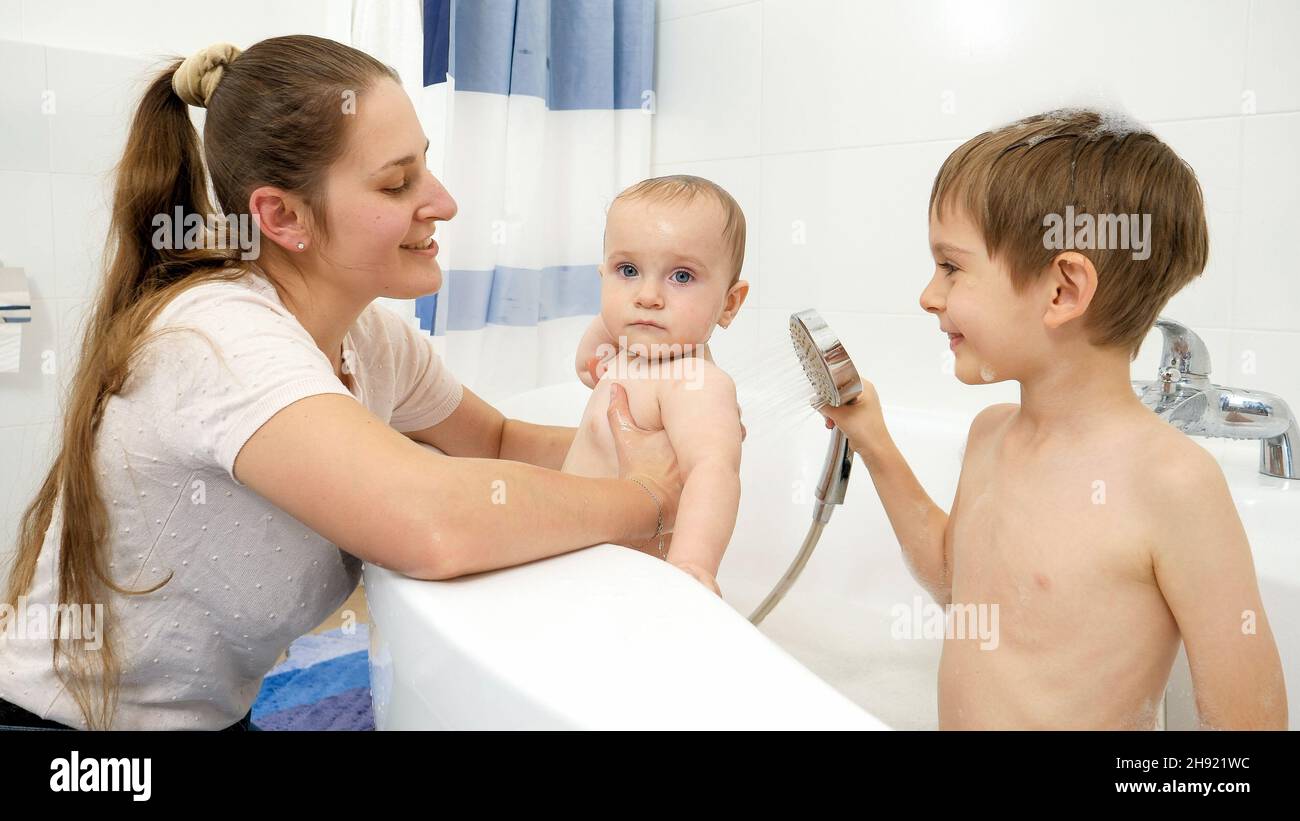 Older boy helping his mother washing baby brother in bath with shower