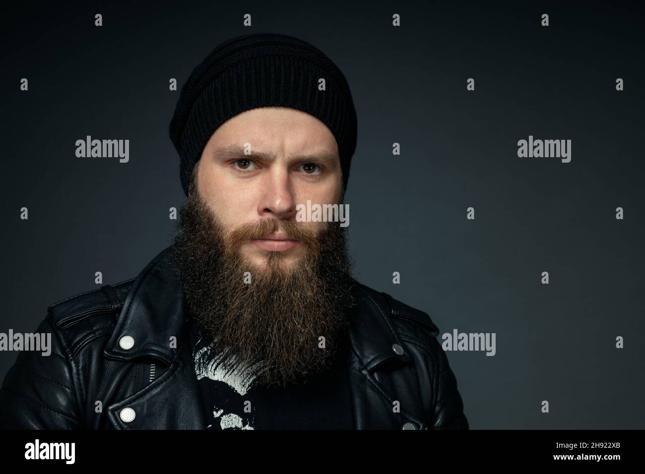 portrait of handsome bearded man in leather jacket and hat looking at the camera. Stock Photo