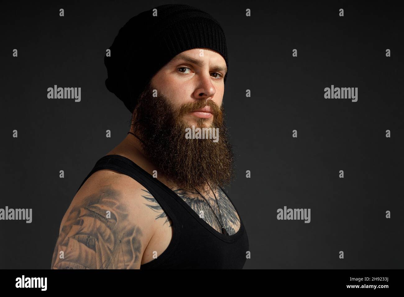 portrait of a handsome bearded man in a black t-shirt and hat looking at the camera. Stock Photo