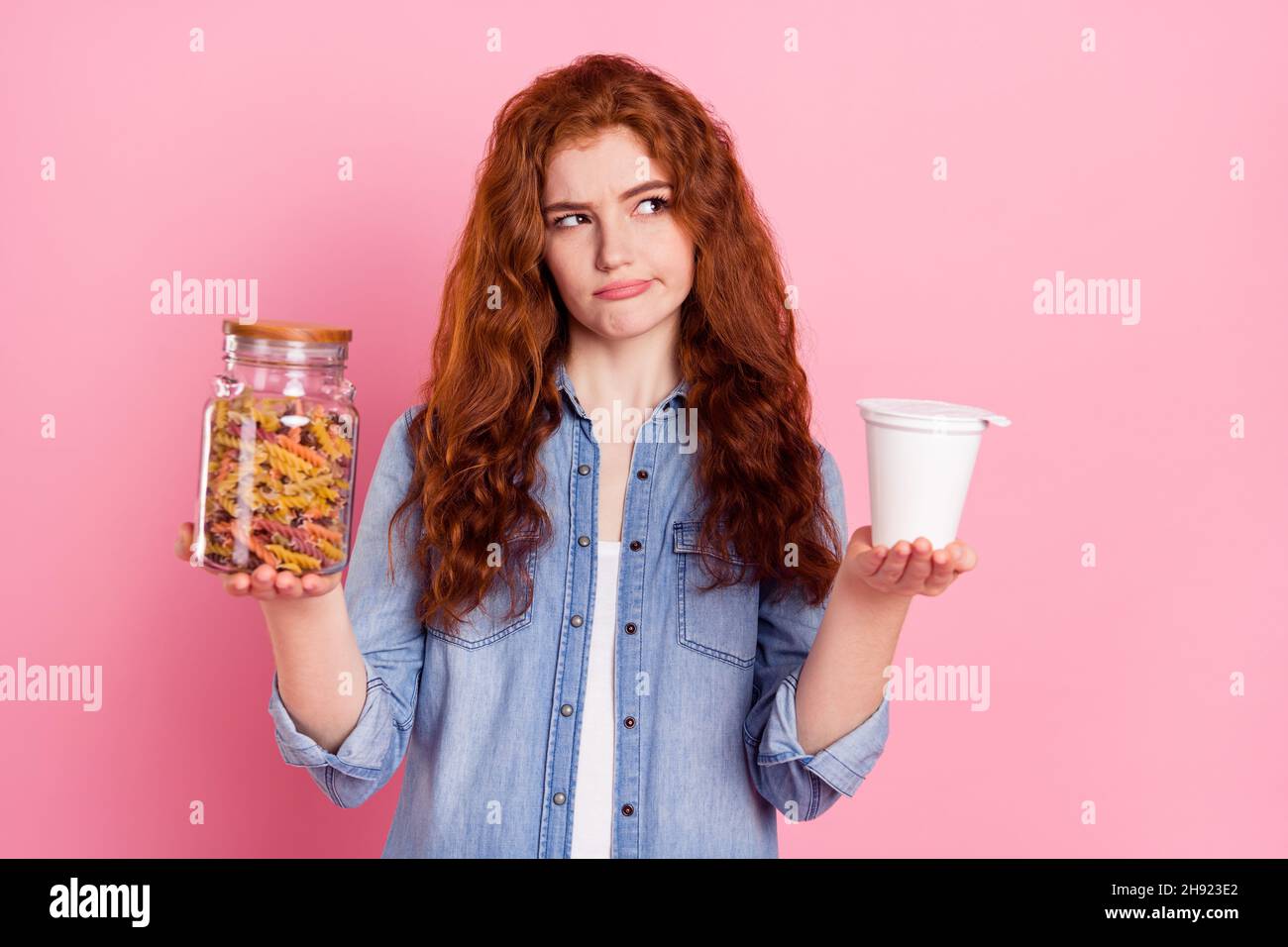 Photo of pretty doubtful woman wear denim shirt choosing organic or junk food looking empty space isolated pink color background Stock Photo