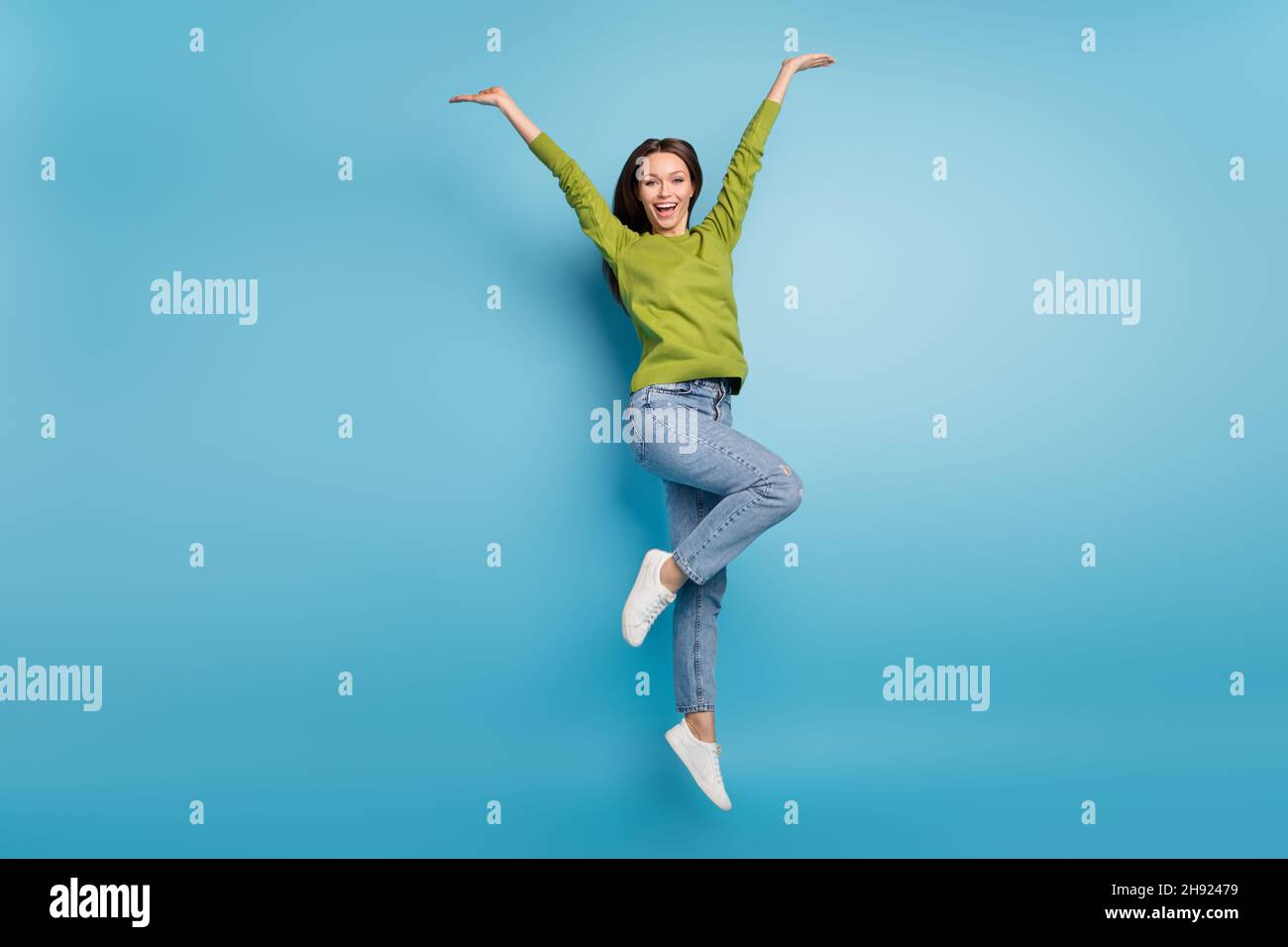 Photo of amazed funny lady jump raise arms wear green shirt jeans footwear isolated blue color background Stock Photo