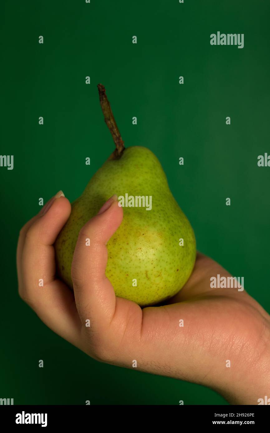 Caucasian hand holding a green pear  with a green background Stock Photo