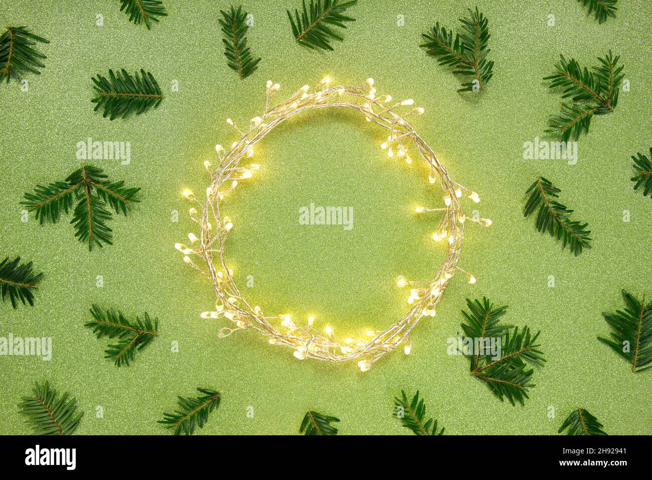 Flat lay top view, Christmas background circle shape border frame, light garland and fir twigs green glitter background. Stock Photo
