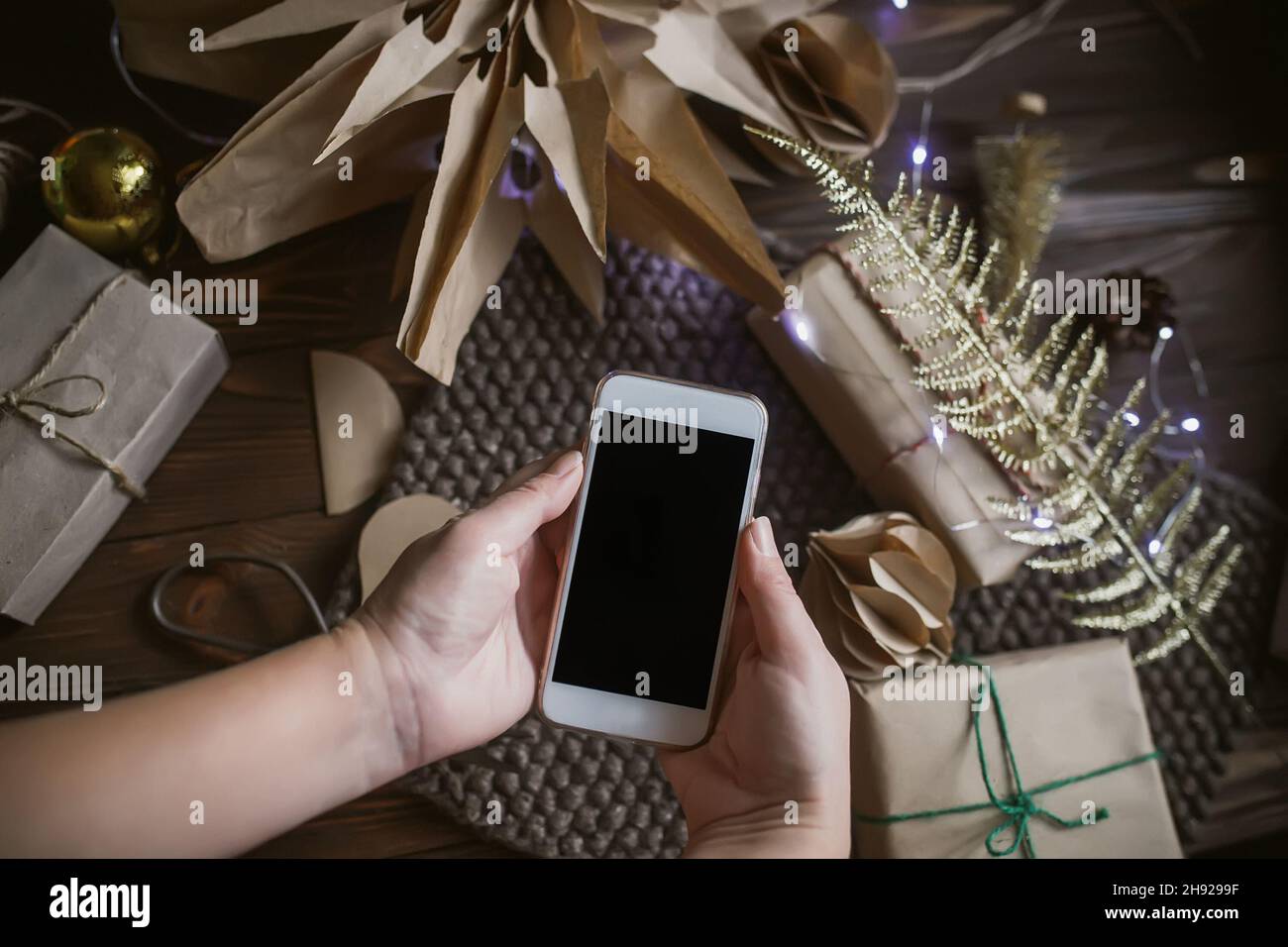Hands holding a mobile phone on the background of Christmas decorations made of recycled materials and paper Stock Photo