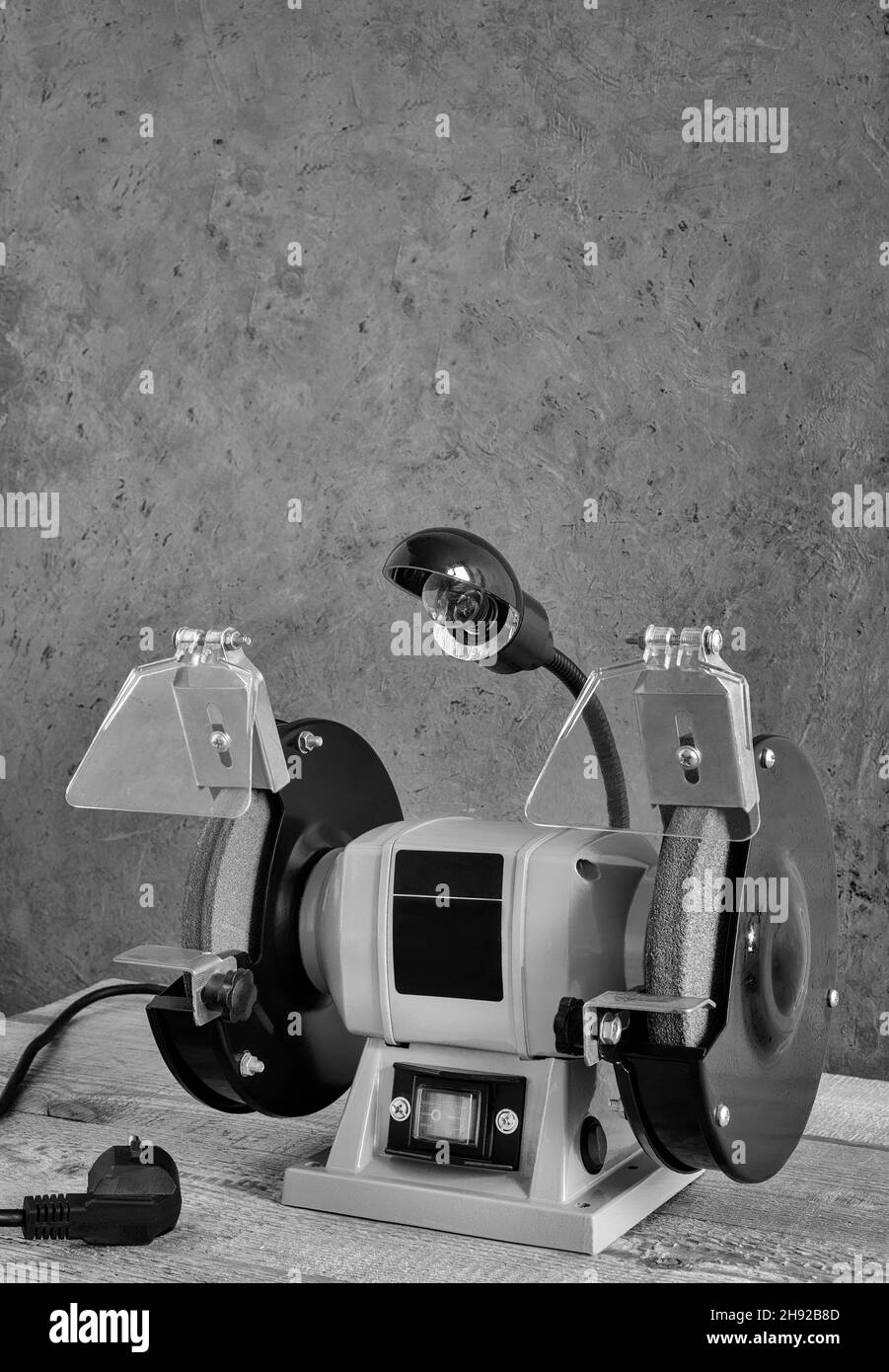 A small electric tool sharpening machine with two grinding wheels, protective casings, protective screens and a lamp. Front view, copy space. Stock Photo