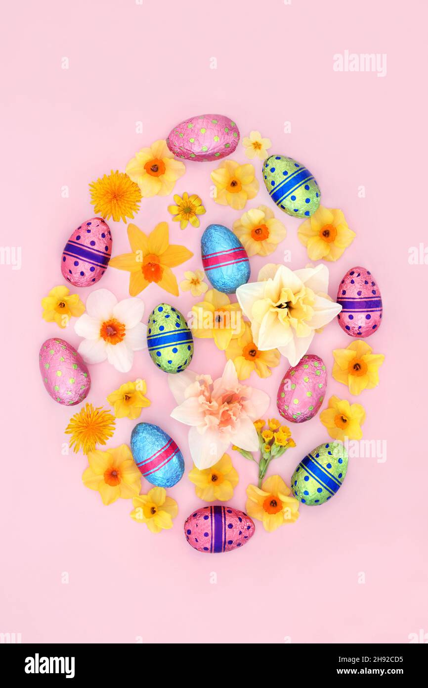 Easter egg concept shape with foil wrapped eggs and spring flowers. Design element for the holiday season on pink background. Top view. Stock Photo