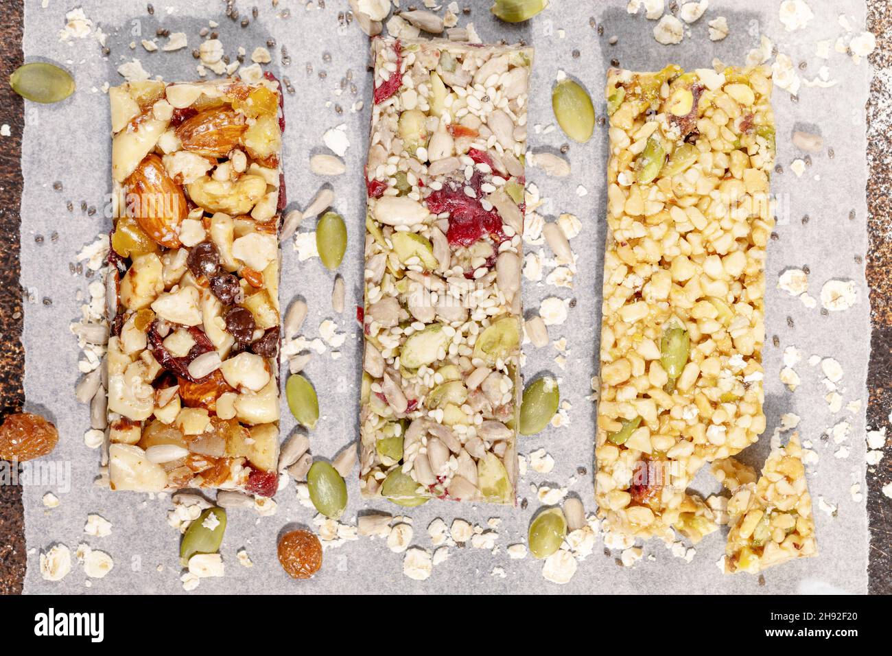 Different kind of granola cereal bars with nuts, seeds, oats, berries and dry fruits on a white pergament paper. Protein muesli bars. Granola superfoo Stock Photo