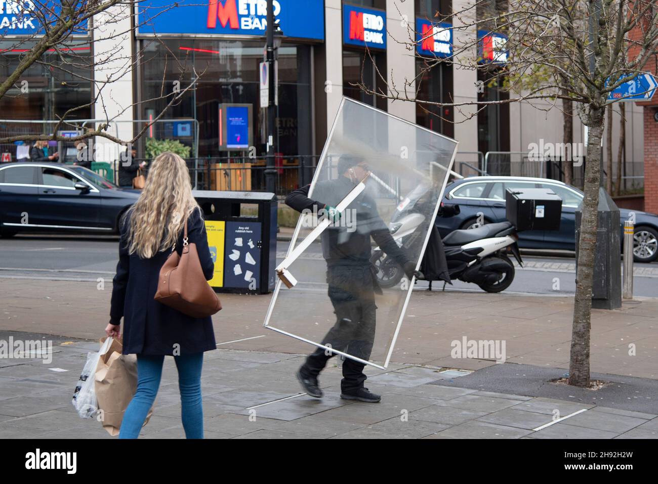 A man carries a sheet of perplex glass along Wimbledon High Street Stock Photo
